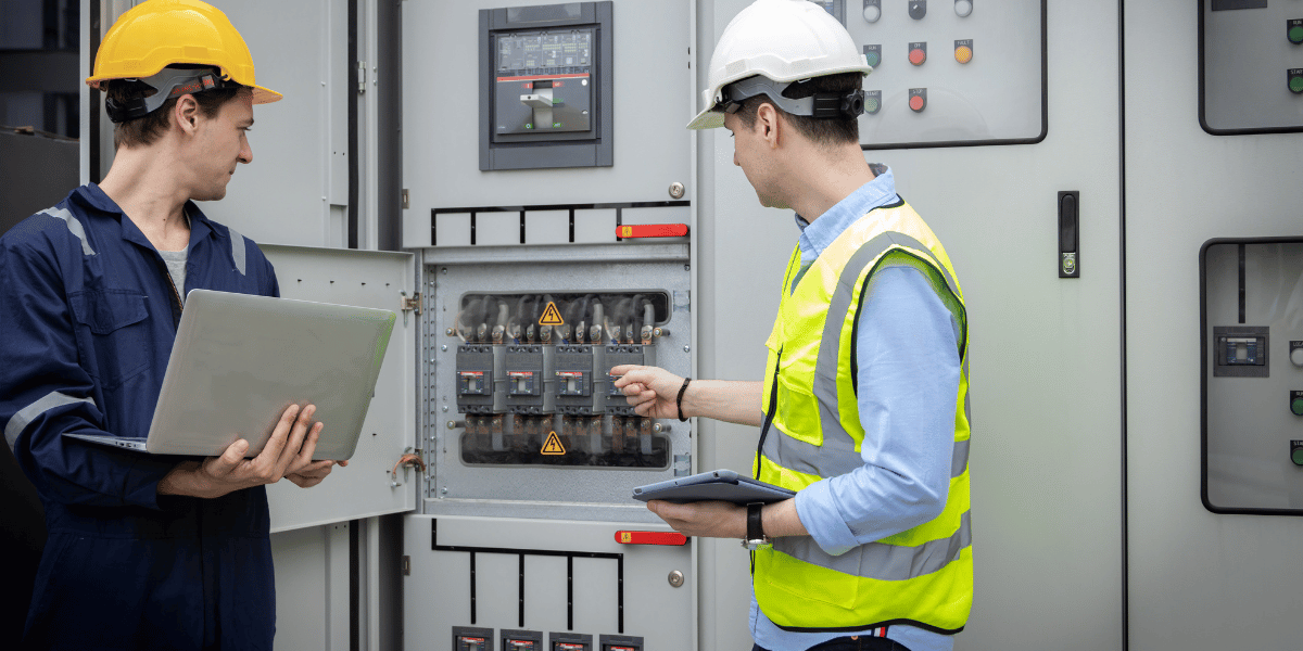 Two male workers in safety gear examining control panel.