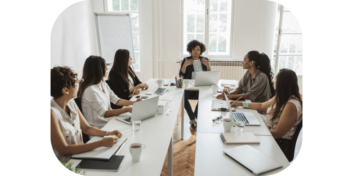 6 women sitting around a table in an office discussing business decisions.